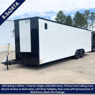 White enclosed tandem-axle trailer with black front, parked in a dealership lot; features include side vents, ramp door, and dual axles.