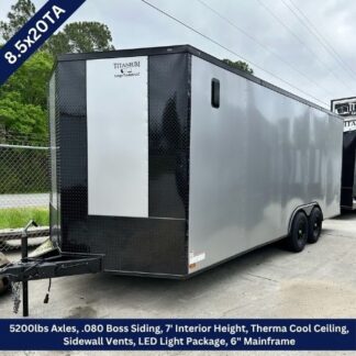 Enclosed cargo trailer on a dealership lot, silver sides with black front, tandem axles and a hitch, ready for towing.