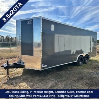 Dark gray enclosed 20-ft cargo trailer with tandem axles on a dirt lot, front hitch visible (8.5x20TA).