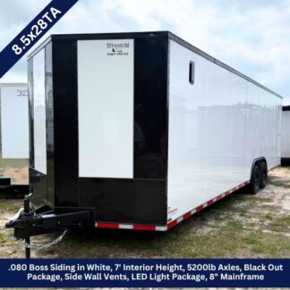 White enclosed cargo trailer with black front panel, tandem axles, and a hitch in a grassy lot.