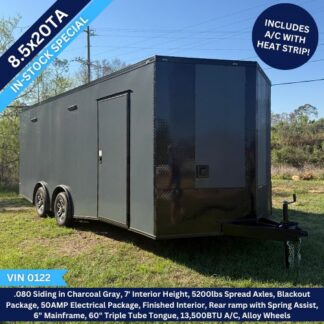 Black 8.5x20TA enclosed trailer on grass with dual axles; features A/C with heat strip, blackout package, finished interior, 50A service, rear spring-assisted door, and VIN 0122.