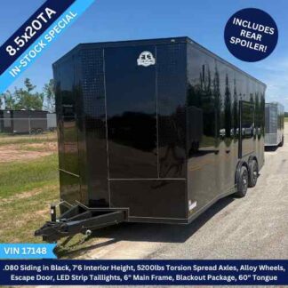 Black 8.5x20TA enclosed cargo trailer with dual axles on a lot; banners advertise in‑stock special and rear spoiler.